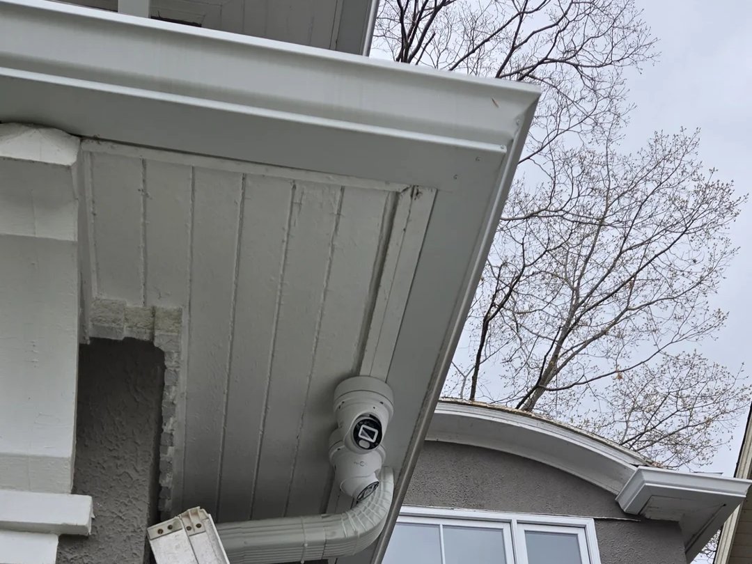Installer on a ladder fitting a security camera at the eave of a Midtown Toronto home